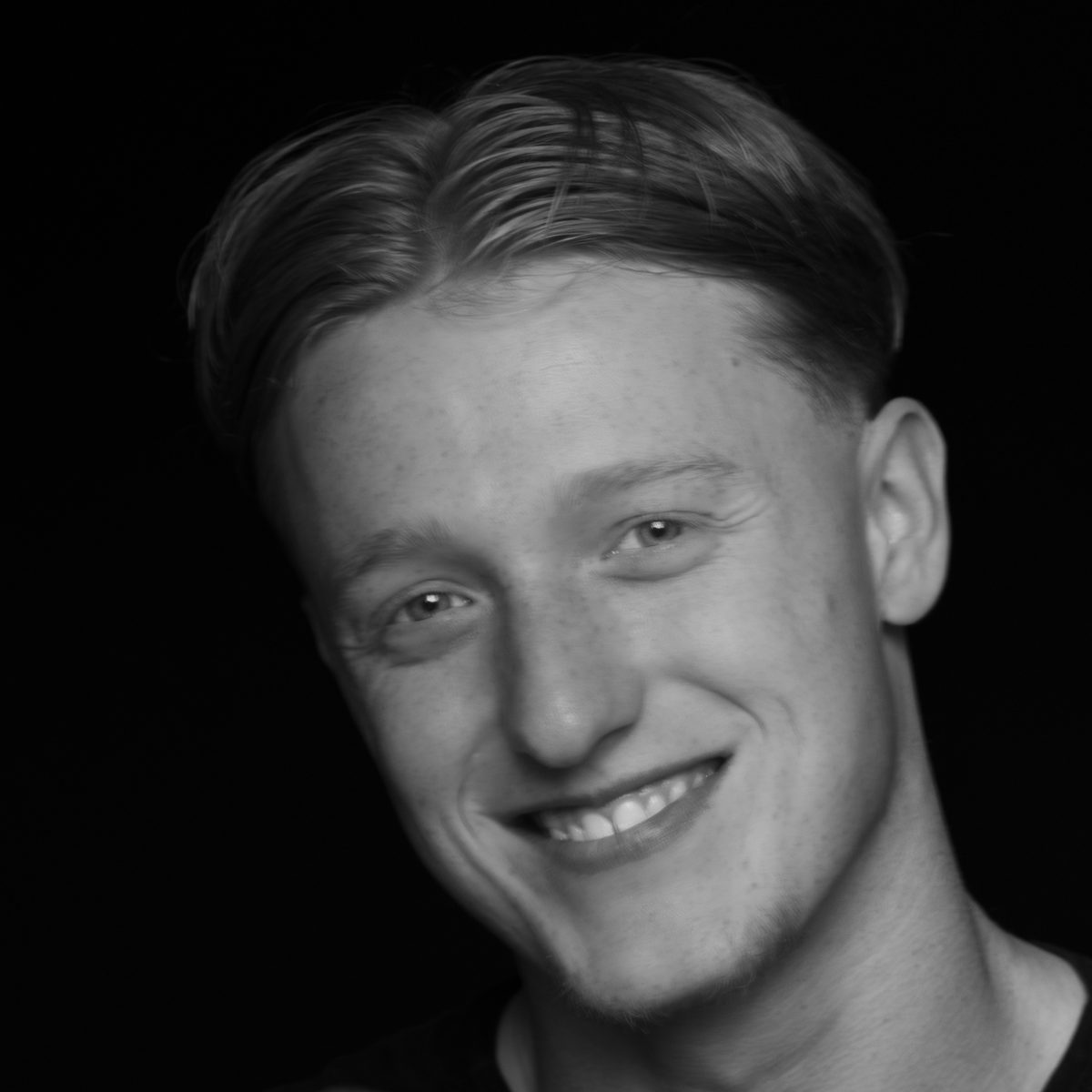 Zwart-witportret van een lachende jonge man tegen een donkere achtergrond